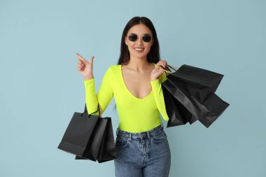 Alışveriş torbaları ile güzel genç Asyalı kadın mavi arka plandaki bir şeyi işaret ediyor. Kara Cuma indirimi