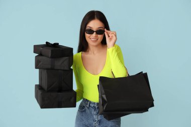 Alışveriş torbaları ve mavi arka planda hediye kutuları olan güzel bir Asyalı kadın. Kara Cuma indirimi