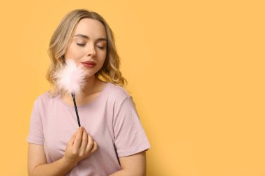 Sarı arka planda tüy çubuğu olan güzel genç bir kadın.