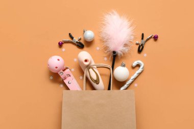 Farklı seks oyuncakları ve turuncu arka planda Noel dekoru olan bir alışveriş çantası.