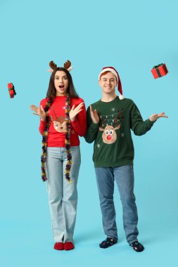 Mavi arka planda Noel süsleri ve hediye kutuları olan genç bir çift.