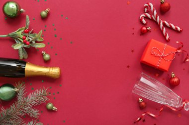 Kırmızı arka planda cam ve Noel dekoru olan şampanya şişesi.