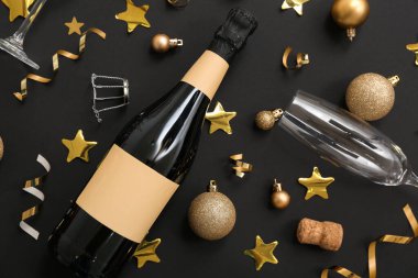 Şampanya şişesi ve siyah arka planda Noel süsü olan bardaklar.