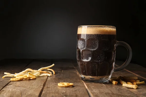 Mug of dark beer and snacks on table against black background