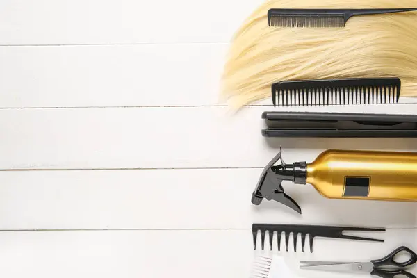 Set of hairdresser's tools and blond strand on white wooden background