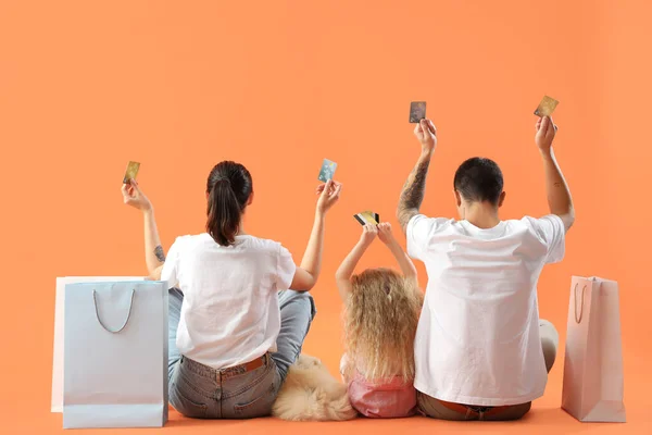 Happy family with credit cards and shopping bags on orange background, back view