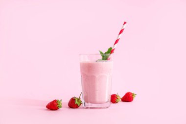 Pembe arka planda bir bardak lezzetli çilekli smoothie.