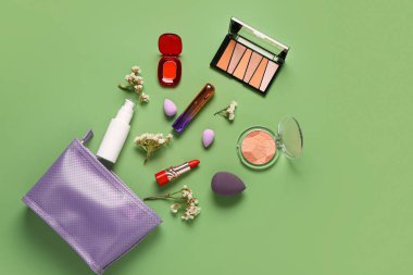 Mor makyaj ürünleri ve yeşil arka planda güzel çiçeklerle süslü şık bir makyaj çantası.