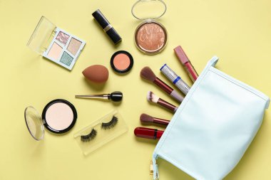 Sarı arka planda makyaj ürünleri olan şık kozmetik çanta