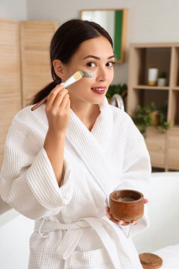 Banyoya yüz maskesi takan genç bir kadın.