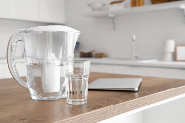 Su filtresi sürahisi, cam ve dizüstü bilgisayar mutfak masasında.