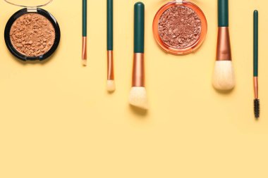 Sarı arka planda makyaj fırçaları ve farklı dekoratif kozmetikler