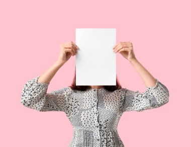 Pembe arka planda boş kağıdı olan genç bir kadın.