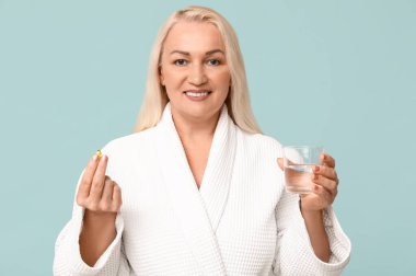 Güzel, olgun bir kadın. Mavi arka planda bir bardak su ve hap.