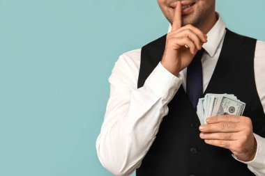 Rüşvetçi genç işadamı mavi arka planda sessizlik jesti sergiliyor.