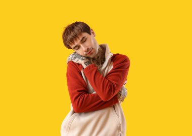 Sarı arka planda kendine sarılan genç adam.