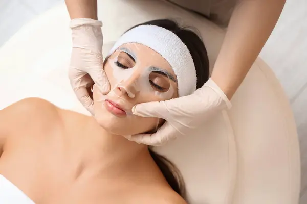 Young woman with facial sheet mask relaxing in spa salon