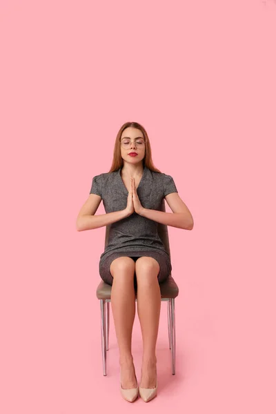 Beautiful young businesswoman sitting on chair and meditating against pink background. Zen concept