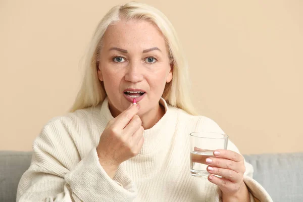 stock image Beautiful mature woman with glass of water taking pill at home