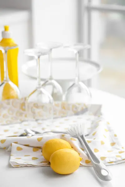 Lemons with cleaning brush and glasses on table in kitchen, closeup