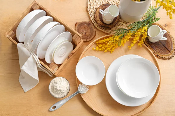 Set of white dishes with cleaning powder and brush on wooden table, top view