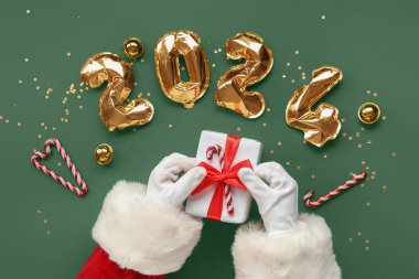 Noel hediyeli Noel Baba elleri, dekorasyon ve 2024 model balonlardan yapılmış renkli arka plan, yakın plan.