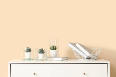 Bej duvarın yanındaki çekmecelerde farklı bitkiler ve kitaplar var.