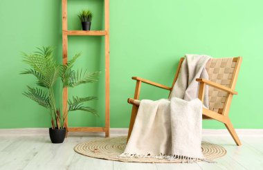 Yeşil duvarın yanında battaniyeli ve çiçekli rahat bir koltuk.