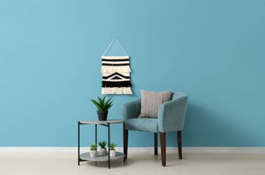 Mavi duvarın yanında farklı bitkiler olan rahat bir koltuk ve kahve masası.