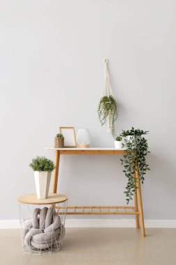 Farklı ev bitkilerine sahip konsol masası, fener ve beyaz duvarın yanındaki boş fotoğraf çerçevesi