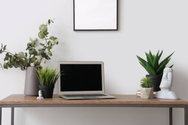 Modern dizüstü bilgisayar ve beyaz duvarın yanındaki masada farklı ev bitkileri.