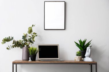 Modern dizüstü bilgisayar ve beyaz duvarın yanındaki masada farklı ev bitkileri.