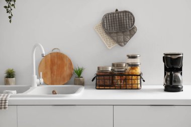 Lavabosu, kavanozu ve kahve makinesi olan beyaz mutfak tezgahı.