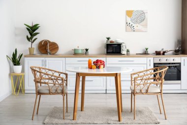 Modern mutfağın içinde meyve sepeti ve yemek masasında bir bardak meyve suyu.