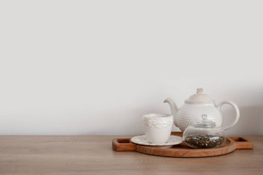 Ahşap mutfak tezgahında çaydanlık, fincan ve çay yaprakları var.