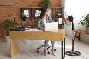 Ofisinde elektrikli yelpazesi olan genç bir iş kadını.