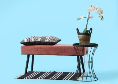 Mavi arkaplanda çiçekler ve minderli pembe bir bank.