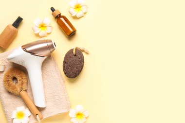 Banyo malzemeleri, kozmetik ürünleri ve sarı arka planda güzel çiçeklerle modern fotoepilatör.