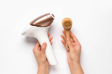 Modern fotoğraf makinesi ve beyaz arka planda masaj fırçası olan kadın elleri.