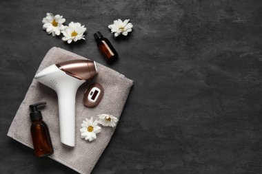 Eklenti, kozmetik ürünler ve grunge siyah arkaplan üzerindeki güzel çiçeklerle modern fotoepilatör.