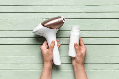 Yeşil ahşap arka planda modern fotoepilatör ve kozmetik ürünü olan kadın elleri