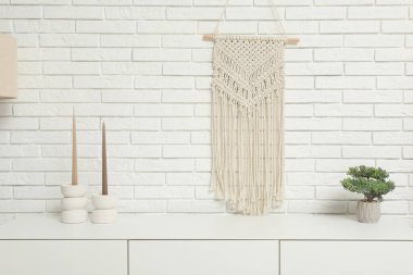 Modern beyaz çekmeceler, mumlar ve beyaz tuğla duvarın yanındaki ev bitkileri.