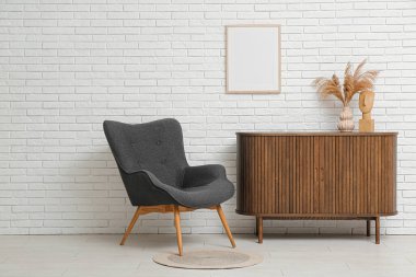 Koltuklu ve beyaz tuğla duvarın yanındaki fotoğraf çerçeveli modern kahverengi çekmeceler.