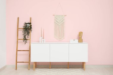 Odadaki pembe duvarın yanında merdivenli ve çiçekli modern beyaz çekmece.