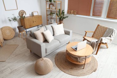 Kahve masasında gri kanepesi, koltuğu ve dizüstü bilgisayarı olan modern oturma odası.