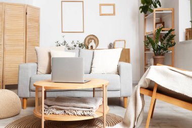 Ahşap sehpada gri kanepe ve dizüstü bilgisayarı olan modern oturma odasının içinde.