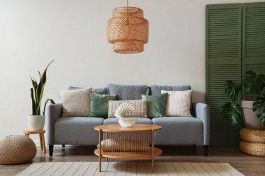 Modern oturma odasının içinde gri kanepe, yeşil katlanmış ekran ve kahve masası.