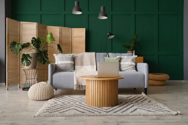 Ahşap sehpada gri kanepe ve dizüstü bilgisayarı olan modern oturma odasının içinde.