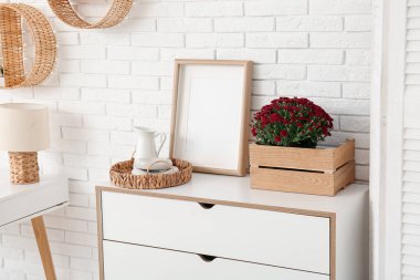 İçinde güzel kasımpatı çiçekleri ve oturma odasındaki çekmecelerin üzerinde boş fotoğraf çerçevesi olan bir kutu.