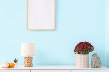 Oturma odasındaki beyaz masada güzel kasımpatı çiçekleri ve balkabakları olan tencere.